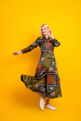 Elegant mature woman in a patchwork dress spinning on yellow background for fashion lifestyle shoot