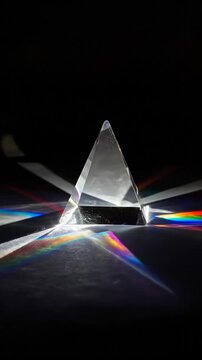 A clear triangular prism refracts light, creating a vibrant spectrum of colors on a reflective surface (1)