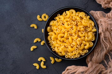 Raw macaroni pasta on black stone background