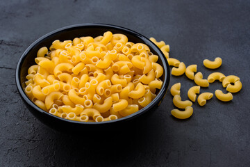 Raw macaroni pasta on black stone background