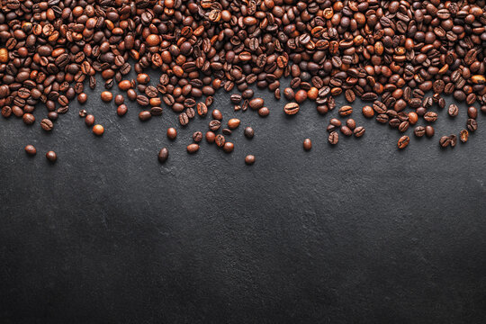 Roasted coffee beans border on dark slate