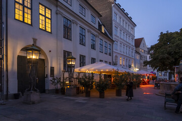 Copenhagen, Denmark - 30 September 2025: View of the illuminated lanterns casting a warm glow on the cobblestone streets and historic buildings, contrasting with the cool twilight sky.