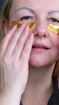 Adorable curly woman glancing straight on camera. Happy woman smiling and using gold eye patches with collagen, peptide, ceramide and hyaluronic acid, derma oil. Dermatology, healthy skin concept.