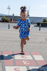 Cute girl playing hopscotch on playground outdoors. Little child playing hopscotch. Active child jumping on playground