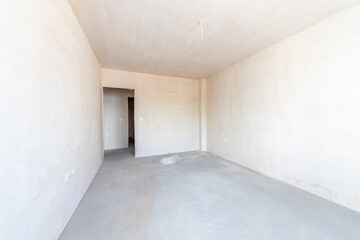 Interior of an empty room under construction in a new apartment. Unfinished space with raw concrete walls, floor, and a large window. Renovation and real estate concept.