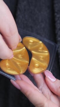 Adorable curly woman glancing straight on camera. Happy woman smiling and using gold eye patches with collagen, peptide, ceramide and hyaluronic acid, derma oil. Dermatology, healthy skin concept.