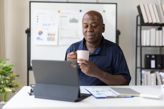 Smiling senior manager drinking coffee and working on a tablet in office. - Powered by Adobe