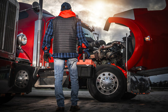 Truck Driver Inspects Engine in Parking Lot During Sunset