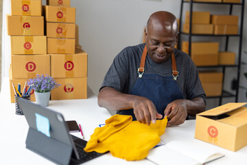 Senior business owner folding yellow clothes preparing sme online orders before sending to client.