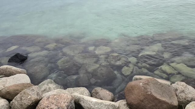 a rocky shoreline leading into clear, shallow and transparent water.some green vegetation is visible.water surface