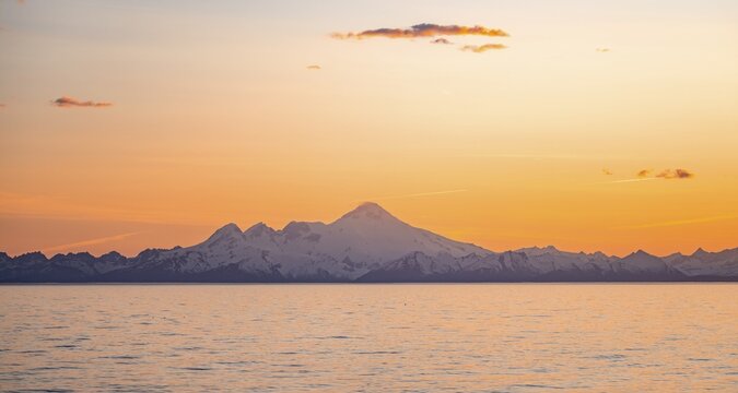 View of Cook Inlet on white mountain peaks of Mount Iliamna at sunset, picturesque golden light of the midnight sun, mountains of the Aleutian Range, Anchor Point, Anchor River State Recreation Area, Alaska, USA