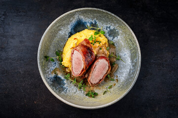 Pork fillet roast wrapped in prosciutto ham bacon with polenta and fresh herbs served as top view in a design bowl