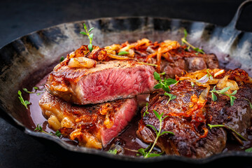 Zwiebelrostbraten roast beef - sirloin beef steak braised with fried onion rings and herbs served in red wine sauce in rustic iron skillet on a wooden board