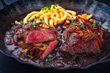 Zwiebelrostbraten roast beef - sirloin beef steak braised with fried onion rings in red wine sauce with spaetzle in rustic iron skillet