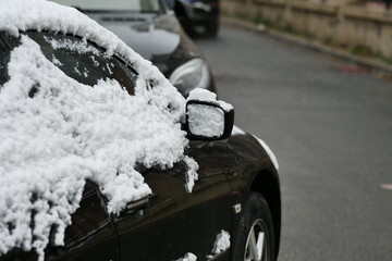 A close-up shot of a car heavily covered in fresh, wet snow on a winter day.