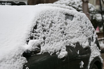 A close-up shot of a car heavily covered in fresh, wet snow on a winter day.