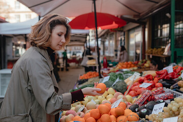 Woman checking orange during street market visit, fresh produce colors, focused gesture, natural daylight over fruit display.
