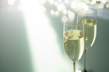 Two elegant champagne glasses filled with sparkling wine and bright blurred bokeh lights in modern setting. Background for sophisticated celebrations. Close-up with space for text.