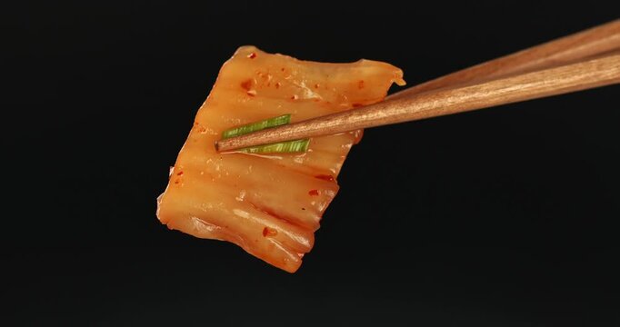 Chopsticks holding kimchi cabbage. Close-up footage on a black background.