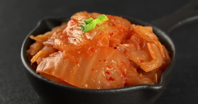 Bowl with korean traditional cabbage kimchi on dark background. Kimchi is garnished with green onions. Close-up footage on the rotating table.