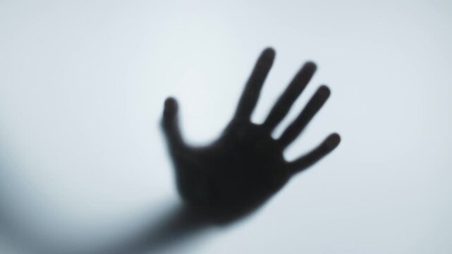 Eerie shadowy figure of a hand gliding across a frosty glass pane. Spooky depiction of a ghostly presence or menacing creature