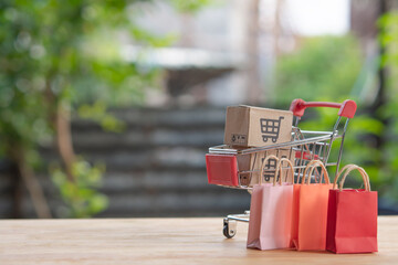 Mini shopping cart with cardboard boxes and colorful shopping bags on wooden table outdoors