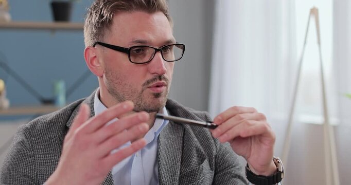 Man psychologist sits in office and listens attentively, holds pen and notebook. Therapist on therapy session.