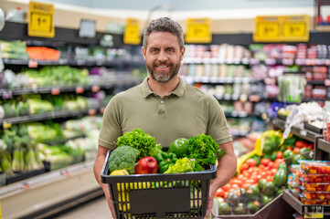 Man shopping with vegetable basket in supermarket. Grocery consumer. Man shopping at grocery store. Healthy lifestyle. Organic food basket. Man in grocery store. Grocery store products
