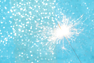 Festive sparkler light with glowing sparks on blue glitter background. Elegant holiday celebration concept ideal for New Year design, greeting cards, banners, marketing materials and promotions
