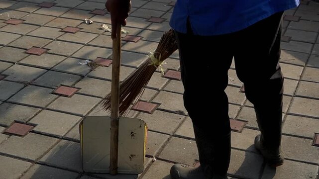 Middle-aged man sweeping fallen leaves with a traditional bidi broom in a park garden during the morning. This peaceful scene of routine maintenance is ideal for background footage