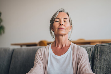 Middle aged woman meditating at home with eyes closed, relaxing body and mind in a living room. Mental health and meditation for no stress concept
