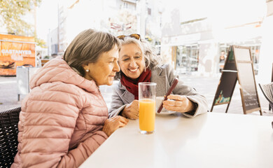 Senior women friends enjoying cafe sharing smartphone