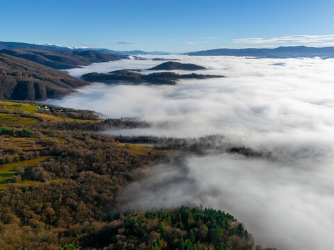 Aerial view of a sea of clouds nestled between rolling hills, with dense forests and open fields adding depth to the landscape, Slovakia.