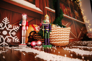 Low-Angle Festive Scene with a Purple and Gold Nutcracker King and a Pink Unicorn Nutcracker, Surrounded by a Woven Basket, Large White Snowflake, Christmas Lights, and Scattered White Beads on a Wood
