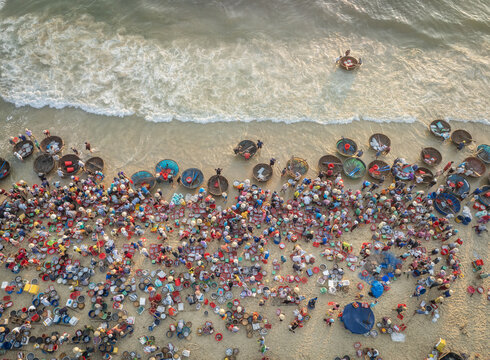 Aerial view of a vibrant gathering of people with colorful baskets on the sandy beach where the sea meets the shore, Tam Tien, Quang Nam, Vietnam