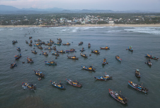 Aerial view of fishing boats scattered across the tranquil water near the shore, reflecting the soft light of the sky, Tam Tien, Quang Nam, Vietnam