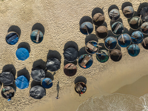 Aerial view of round boats scattered like fallen leaves along the sandy shore where the turquoise sea meets the golden beach, Tam Tien, Quang Nam, Vietnam