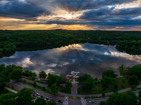 Aerial view of the glistening Fresh Pond Reservation reflecting the dramatic sky, with lush trees and the Cambridge Boat Club, Boston, Massachusetts, United States.