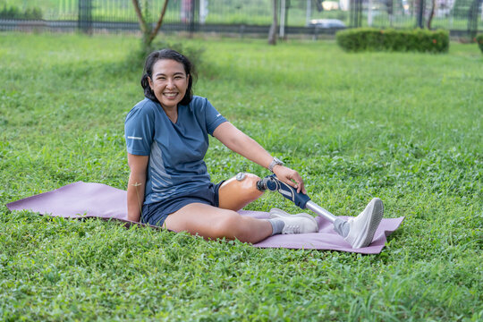 asian woman with prosthetic leg in sportswear sitting on yoga mat in the park
