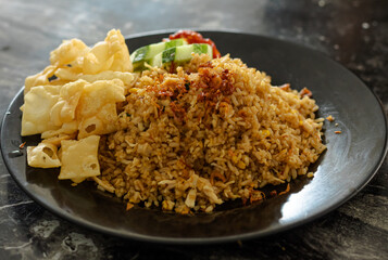 Indonesian fried rice Nasi Goreng served with fried wonton skins, cucumber, and chili sauce on a dark plate.