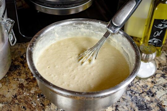 Perfectly mixed, smooth waffle batter rests in a silver bowl with a whisk, waiting for the waffle iron to preheat before cooking in Waukesha County, Wisconsin.
