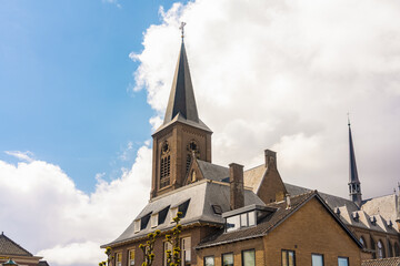 View of a towering brick church with a dark spire reaching into the bright blue sky dotted with fluffy white clouds, Noordwijk, South Holland, Netherlands.