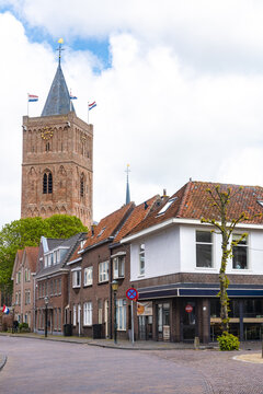View of an old brick tower topped with flags rises above quaint buildings with orange tiled roofs under a sky with fluffy clouds, Noordwijk, South Holland, Netherlands.