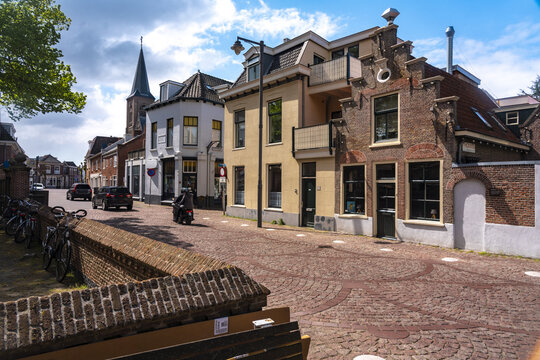 View of brick-paved street winding past quaint buildings under a partly cloudy sky, with parked bicycles and the spire of a church, Noordwijk, South Holland, Netherlands.