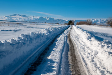 A serene snowy pathway stretches across a bright landscape with majestic mountains in the background, showcasing the tranquility of winter's beauty in nature.