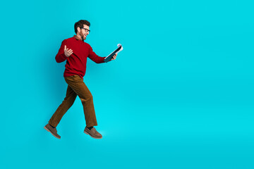 Young stylish man in a red sweater jumps notebook blue background for a dynamic lifestyle and...