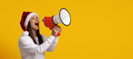 A young woman wearing a Santa hat enthusiastically uses a megaphone to spread holiday joy. The...