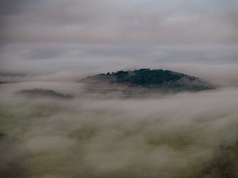 Aerial view of a verdant land mass enveloped in a thick blanket of fog, obscuring the landscape below, Gloucester, Massachusetts, United States.