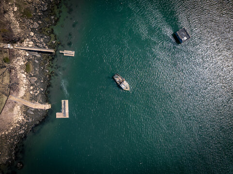 Aerial view of a weathered boat adrift in the deep blue harbor waters near rocky shores and docks, Gloucester, Massachusetts, United States.