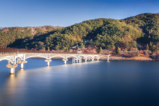 View of the graceful, arched bridge stretching across the tranquil waters, leading to a pagoda nestled in the lush green hills, Andong si, Gyeongsangbuk do, South Korea.